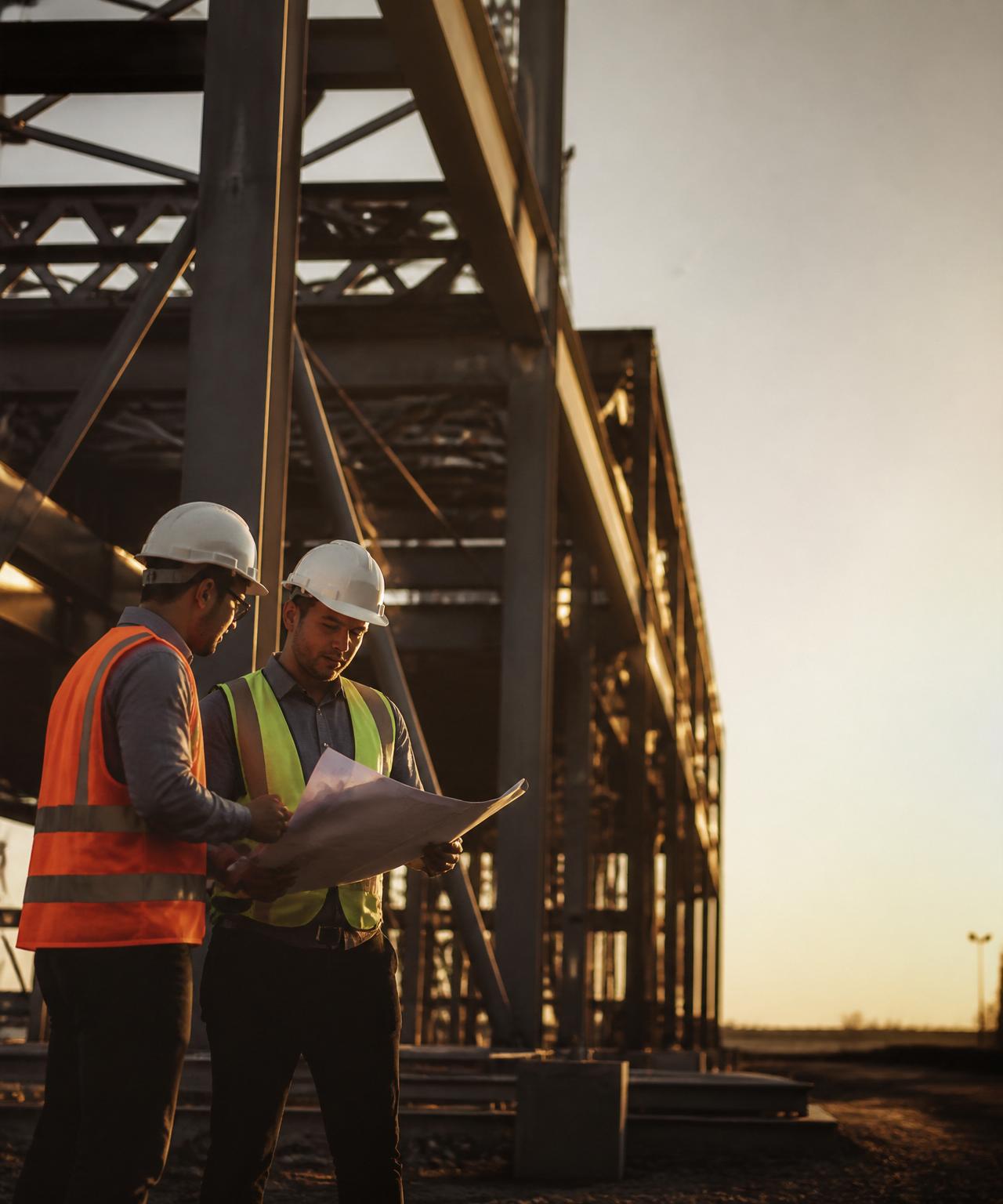 Engineers reviewing plans in front of a steel structure at sunset